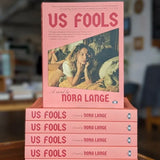 Us Fools a novel by Nora Lange, front cover of book on top of a stack of books